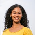 Attractive young woman smiling at camera. Portrait of beautiful cheerful young woman in yellow t-shirt standing on street and smiling at camera. Emotion concept